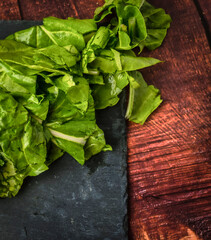 Stilleben mit gesundem Gemüse, frisch gewaschenem Mangold auf braunem Holzhintergrund und schwarzem Teller.