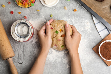 Woman holding unbaked cookie with candied fruits at grey table, top view