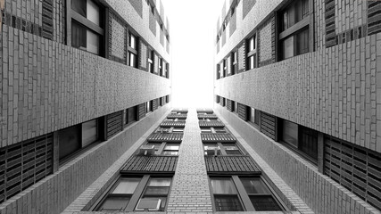 Abstract black and white architecture. Looking upward in the courtyard of a Bronx tenement building toward an overexposed sky. 10mm wide angle, 16:9 aspect ratio. Fine art photography.