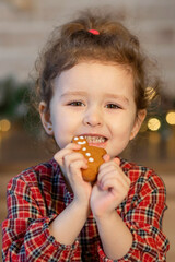 funny little girl eating gingerbread man cookie for new year. happy cute girl with traditional...