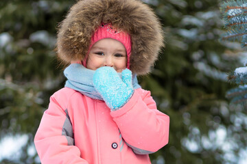 Funny little toddler girl in pink jumpsuit playing in snowballs. wintertime for children. winter games outdoors. Kid having fun at Christmas time