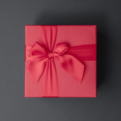 Red gift box with a bow on a dark gray background. Square format. greeting card