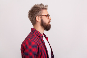 Profile portrait of confident serious bearded guy in eyeglasses and checkered shirt attentively looking right. Indoor studio shot isolated on gray background © khosrork