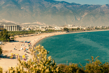 View from above of a large beach with blue sea water greenery and a mountain range in the sea haze in the background