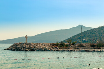 A small lighthouse on a rock ridge in the bay of the town of Kalkan. Mountains in the sea haze on the background
