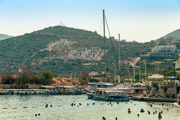 View of the small bay and a part of the town of Kalkan with yachts, people swimming and mountains in the sea haze on the background