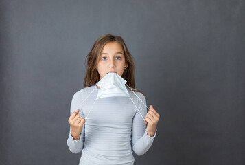 Portrait of a young scared girl playing with medical mask on grey background. - 463831479