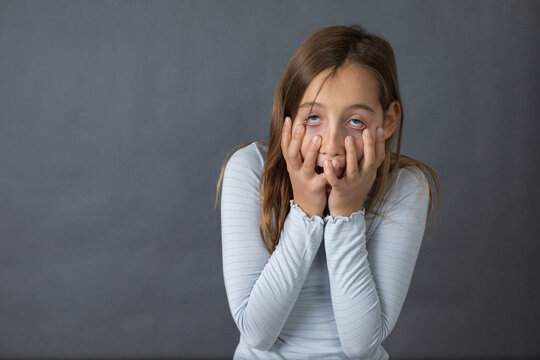 Portrait of a young sad and scared girl on grey background with space for text