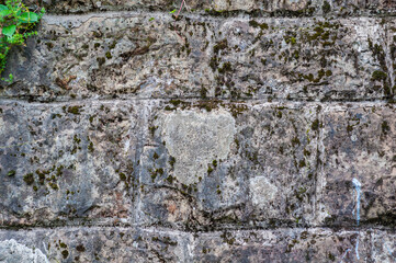 Very old wall building is made stone blocks different sizes, antique surface has been affected by time, rough texture stone