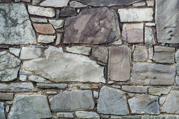 Very old wall building is made stone blocks different sizes, antique surface has been affected by time, rough texture stone
