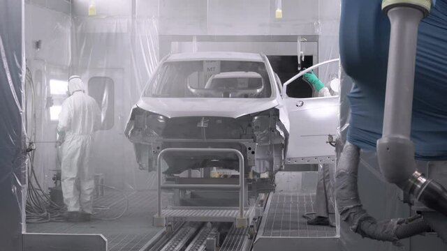 Painting vehicle parts in sprcial booth. Car manufacturing factory. Two painters spray white paint on a bumper car.
