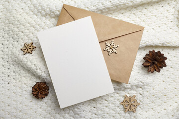 Christmas greeting card mockup with envelope, wooden snowflakes decorations and pine cones on knitted background