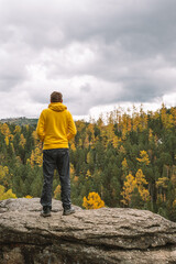 Male traveler in a yellow hoodie stands on top of mountain, admiring the magnificent landscape of...