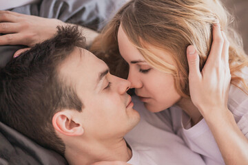 Fototapeta na wymiar Close up portrait of young attractive romantic couple hugging and kissing, laying down on a bed, being loving with each other. Love and relationships lifestyle