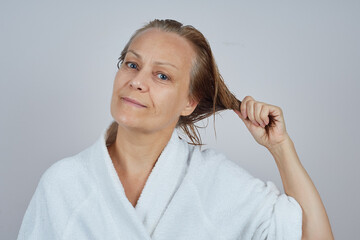 Mature woman in white bathrobe with wet hair after shower