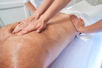 Fototapeta na wymiar Two masseuses massaging male back in spa salon