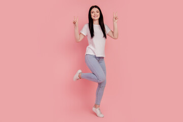 Fototapeta na wymiar Photo of positive cheerful glad casual brunette lady show v-sign stand one leg isolated on pink color background