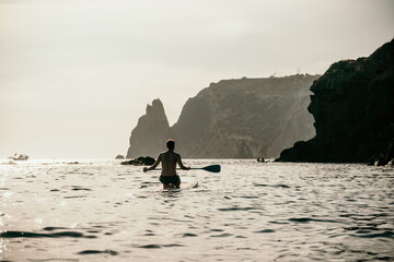 Side view foto of a man swiming and relaxing on the sup board. Sportive man in the sea on the Stand...