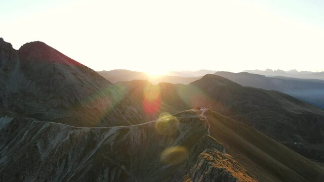 sunrise in the alps, warm light hits the mountain peaks, sunflare. drone flies over the valley and a mountain hut. aerial panoramic view to enjoy.
