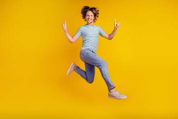 Fototapeta na wymiar Full size photo of young cheerful man happy positive smile jump show fingers rock sign isolated on shine yellow background