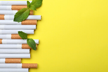 Menthol cigarettes and mint on yellow background, flat lay. Space for text