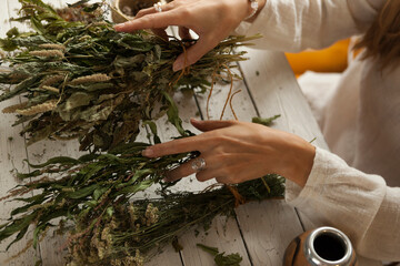  bunch of dried medicinal herbs in women's hands,  collection of medicinal herbs, white wooden table