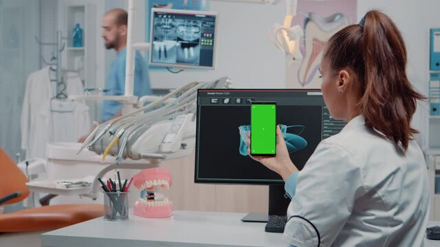 Woman looking at green screen on mobile phone for stomatological care at dentistry office. Orthodontist holding smartphone with chroma key and mockup template on display for teethcare