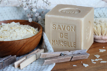 Marseille soap bar named Savon de Marseille in french and grated soap on the cotton towel with clothes pegs and washing brush at home laundry close up.  - obrazy, fototapety, plakaty