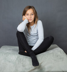 Portrait of a young girl sitting on pillow on grey background with hand on her face - 463842800