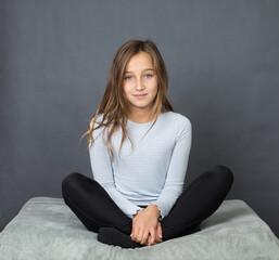 Portrait of a young girl sitting on pillow on grey background with space for text - 463842801