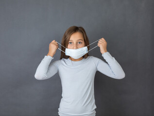 Portrait of a young girl puttin on medical mask on grey background. - 463842808