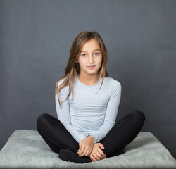 Portrait of a young beautiful girl with brown hair sitting on pillow on grey background with space for text - 463842810
