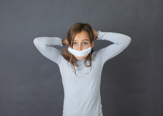 Portrait of a young girl puttin on medical mask on grey background. - 463842815