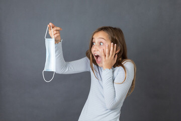 Portrait of a young scared girl holding medical mask on grey background. - 463842817