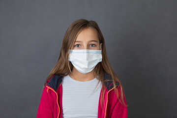 Portrait of a young girl with read sweater in a medical mask lookig in to camera on grey background. - 463842820