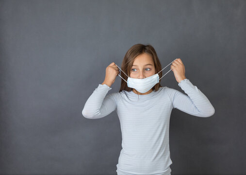 Portrait of a young girl puttin on medical mask on grey background.