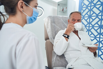 Man drinking coffee and talking with doctor in clinic