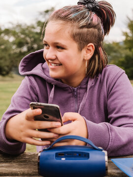 Cheerful teenage girl browsing smartphone near portable speaker in nature