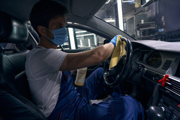 Male in overalls wiping steeping wheel with dry cloth