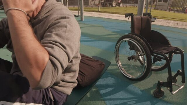 Tracking Out From Wheelchair To Caucasian Man Doing Abs Exercise On Equipment On Sportsground In Neighborhood In Summer Morning