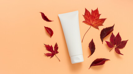 Unbranded white tube of cream or lotion with autumn leaves. Bottle with body lotion or facial cream, tube for cosmetics products template. Autumn skincare, orange background, top view