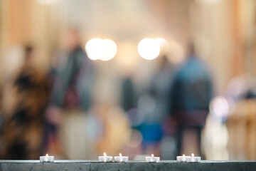 Candles in the church and some blurry people in the background. Sunny, warm colors.