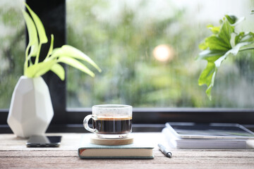 coffee glass cup and diary notebook and plants pot on wooden table with window view