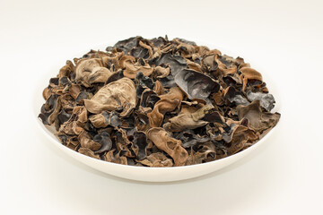 Dried Auricularia mushrooms lie in a round plate, on a white table.