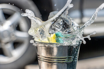 A sponge fall down to bucket with splash of detergent. Hand washing car with soapy water.