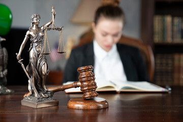 Young female lawyer during work in chamber. Gavel and Themis statue  on the brown shining desk.