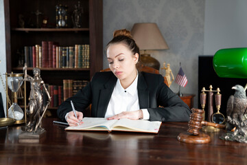 Young female lawyer during work in chamber. Gavel and Themis statue  on the brown shining desk.