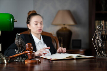 Young female lawyer during work in chamber. Gavel and Themis statue  on the brown shining desk.