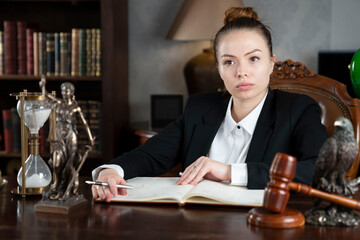 Young female lawyer during work in chamber. Gavel and Themis statue  on the brown shining desk.