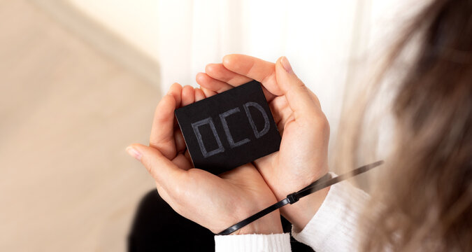 Woman holding black card written OCD and hands are teid with plastic handcuff. Concept of OCD obsessive compulsive disorder.